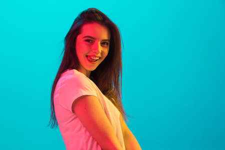 Portrait of young beautiful girl isolated on blue background in neon light.