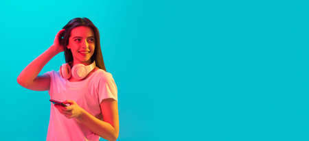 Young beautiful girl with smartphone isolated on blue background in neon light