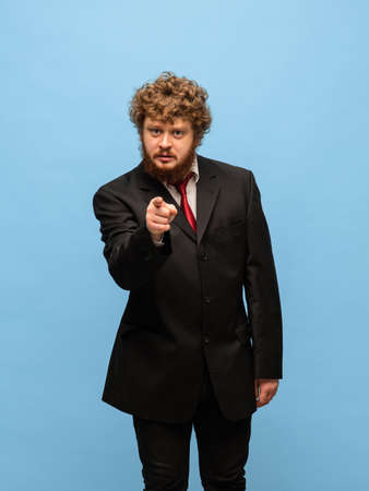 Portrait of young red-headed man in black suit isolated over blue background.の写真素材