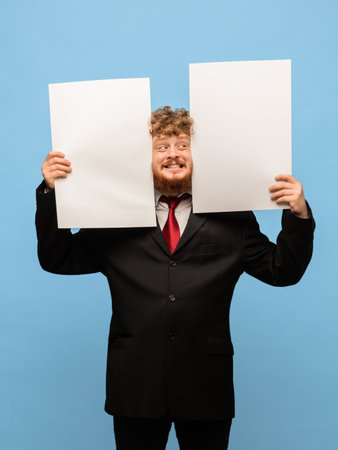 Young red-headed man in black suit holding two blank sheets of paper .の写真素材