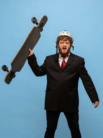 Funny red-headed man in black suit holding longboard isolated on blue backgroundの写真素材