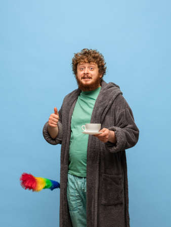 Red-headed man in bathrobe with cup of coffee isolated on blue background