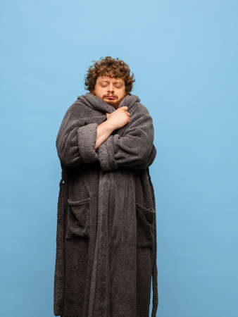 Caucasian man in bathrobe with cup of coffee isolated on blue backgroundの写真素材