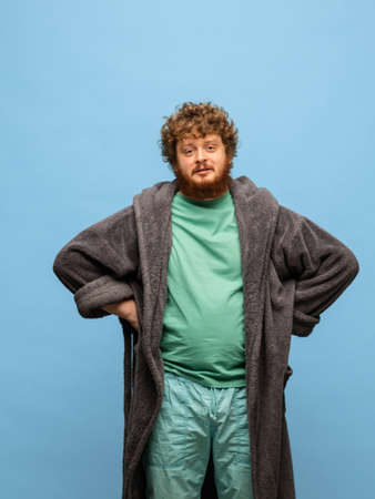 Portrait of Caucasian man in grey bathrobe standing isolated on blue backgroundの写真素材