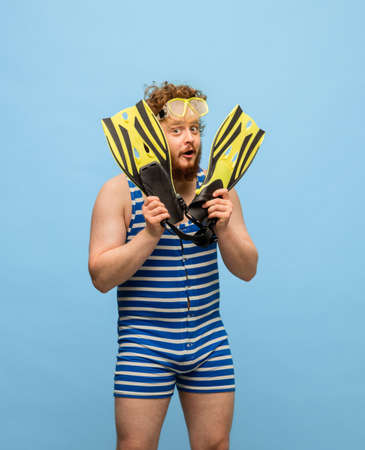 Funny red-headed man in swimming suit and goggles isolated on blue background.の写真素材