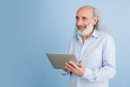 Portarit of senior grey-haired man using tablet isolated over light background.