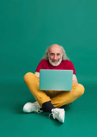 Senior grey-haired man using laptop isolated over green background.の写真素材