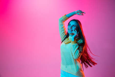 Young beautiful girl talking on phone isolated on pink background in neon lightの写真素材