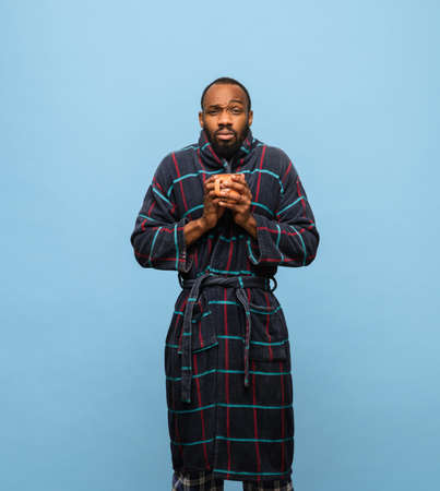 African-American man in bathrobe with cup of coffee isolated on blue backgroundの写真素材