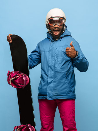 Happy man snowboarder with snowboard in ski suit isolated on blue backgroundの写真素材