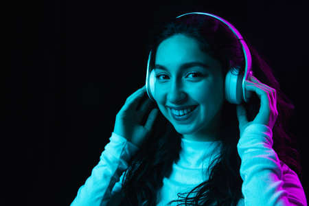 Young beautiful girl in headphones isolated on dark background in neon lightの写真素材