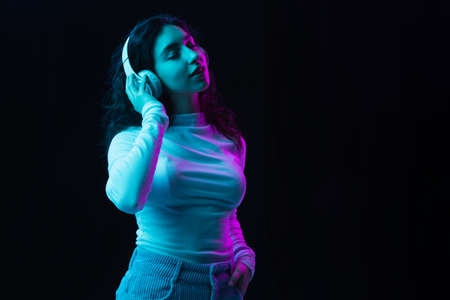Young beautiful girl in headphones isolated on dark background in neon lightの写真素材