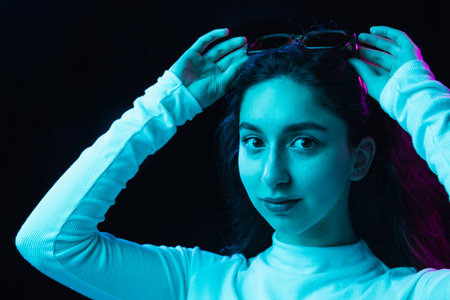 Portrait of young beautiful girl isolated on dark background in neon lightの写真素材