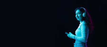Young beautiful girl in headphones isolated on dark background in neon lightの写真素材