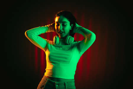 Young Caucasian beautiful girl isolated on dark colored background in neon light