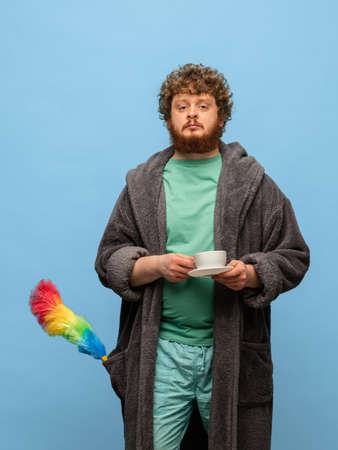 Red-headed man in bathrobe with cup of coffee isolated on blue background