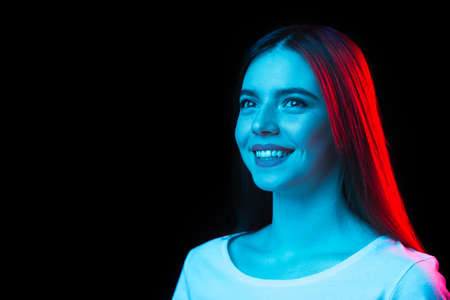 Portrait of young beautiful girl isolated on dark background in neon lightの写真素材