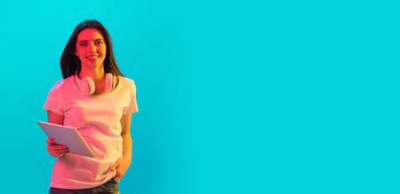 Young beautiful girl using device isolated on blue background in neon lightの写真素材