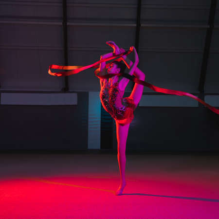 Graceful Caucasian girl gymnast isolated over colored background in neon lightの写真素材