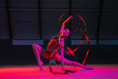 Young female rhythmic gymnast isolated on multicolored background in neon lightの写真素材