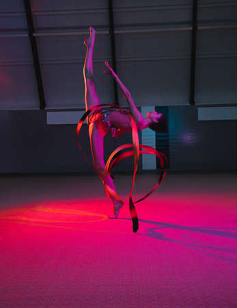 Young graceful girl gymnast isolated over colored background in neon lightの写真素材