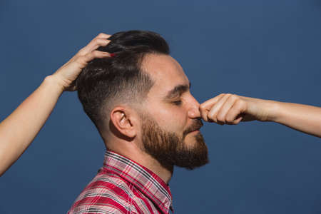 Female hands making different emotions of young bearded man on blue backgroundの写真素材