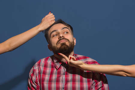 Female hands pulling on hair of young bearded man on blue backgroundの写真素材