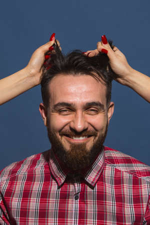 Female hands rumple young bearded handsome man on blue backgroundの写真素材