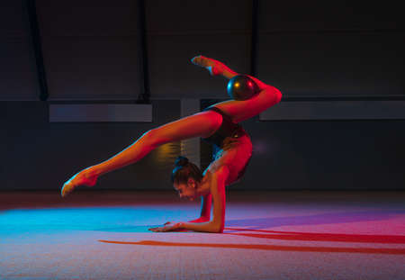 Young graceful girl rhythmic gymnast isolated on dark background in neon light
