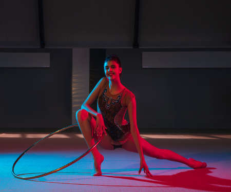 Young graceful girl rhythmic gymnast isolated on dark background in neon lightの写真素材
