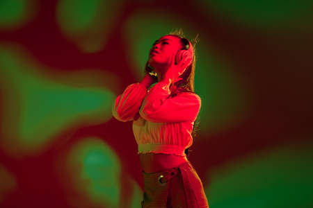 Young Asian girl in headphones isolated over red green in neon light background.