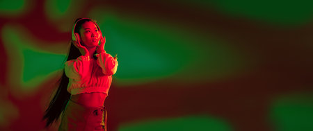 Young Asian girl in headphones isolated over red green in neon light background.