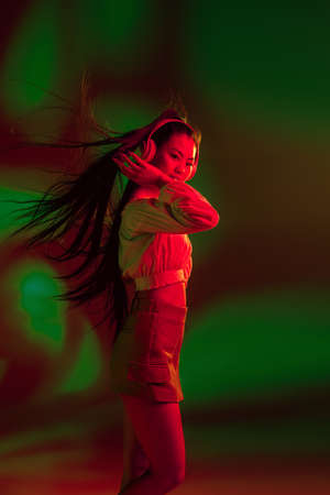 Young Asian girl in headphones isolated over red green in neon light background.の写真素材