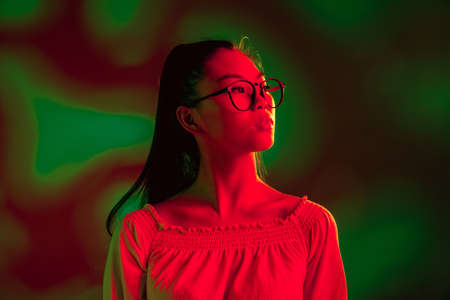 Young beautiful Asian girl isolated over red green neon light background.の写真素材