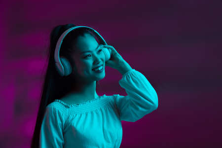 Portrait of pretty young Asian girl isolated on purple background in neon light.