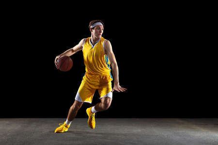 Young Caucasian basketball player training isolated on black background.