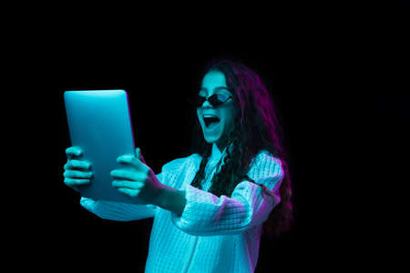 Young beautiful girl with tablet isolated on dark background in neon light