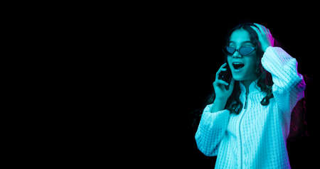 Young beautiful girl talking on phone isolated on dark background in neon lightの写真素材