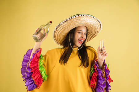Young pretty girl in bright garment and sombrero isolated over yellow backgroundの写真素材