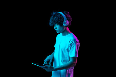 Portrait of young man using tablet isolated over dark background in neon lightの写真素材