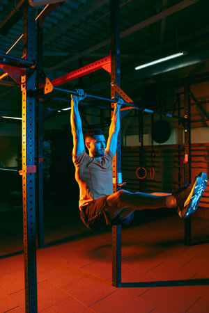 Young athletic man, fitness instructor training in gym in mixed neon light.