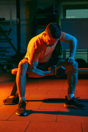 Young athletic man, fitness instructor training in gym in mixed neon light.の写真素材