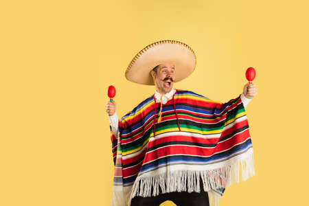 Happy man in sombrero and bright poncho isolated over yellow backgroundの写真素材