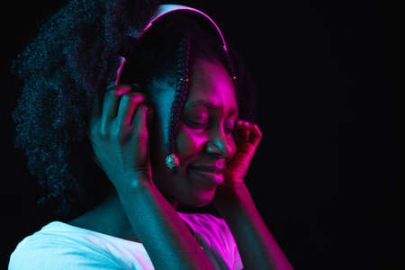Young beautiful African-American girl isolated on dark background in neon light