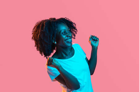 Young beautiful happy African-American girl isolated on pink background in neon.