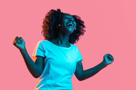 Young beautiful happy African-American girl isolated on pink background in neon.の写真素材