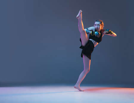 Young female MMA fighter training isolated over blue background in neon lightの写真素材
