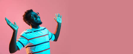 Young African-American man isolated on pink background in neon lightの写真素材