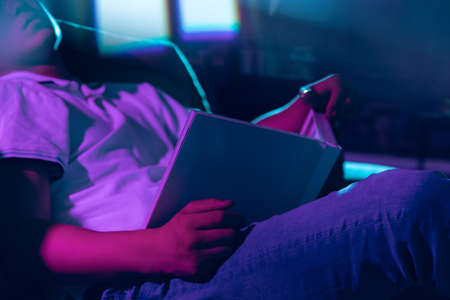 Close-up young man with book at home interior in gradient pink blue neon lightの写真素材