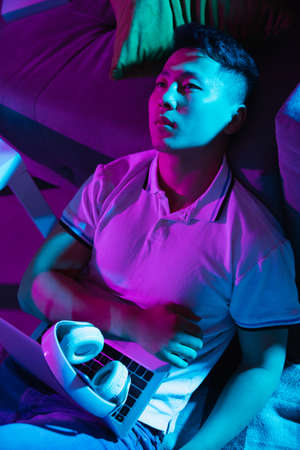 Portrait of young Korean man isolated at home interior in gradient blue neon lightの写真素材